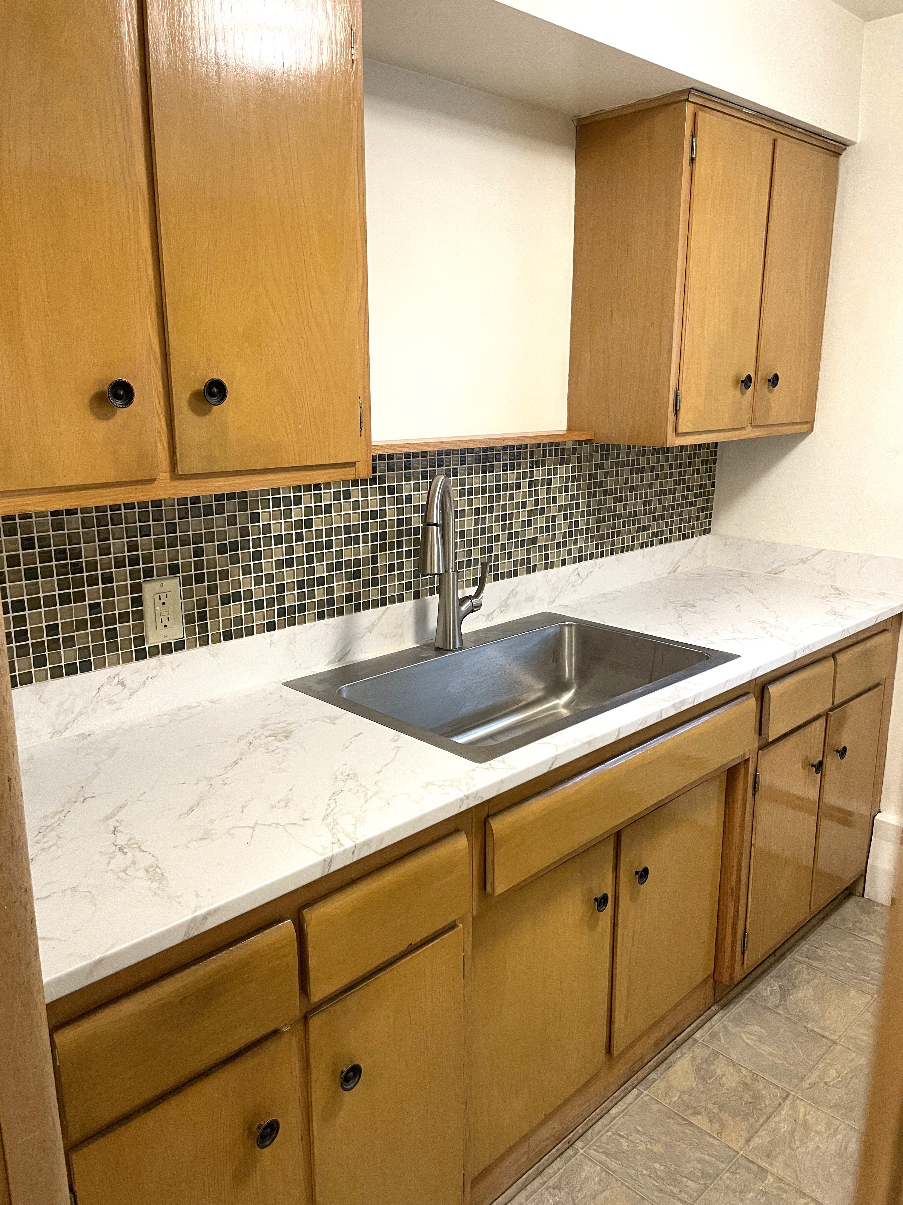 Upgraded kitchen with new countertops, sink, faucet, and attractive mosaic tiled backsplash.